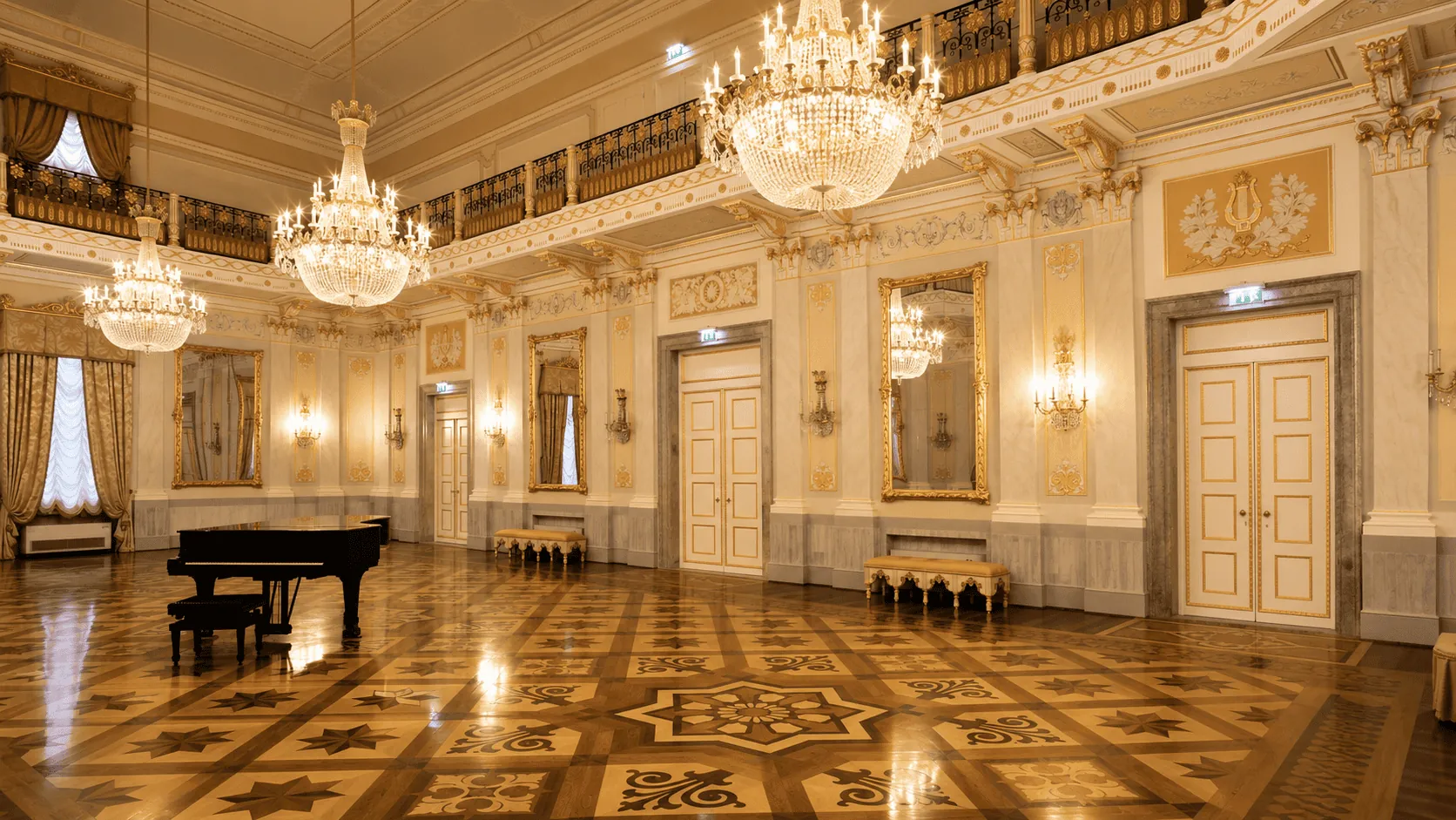 Una sala dorata del teatro con i lampadari in cristallo accesi e un pianoforte a coda.